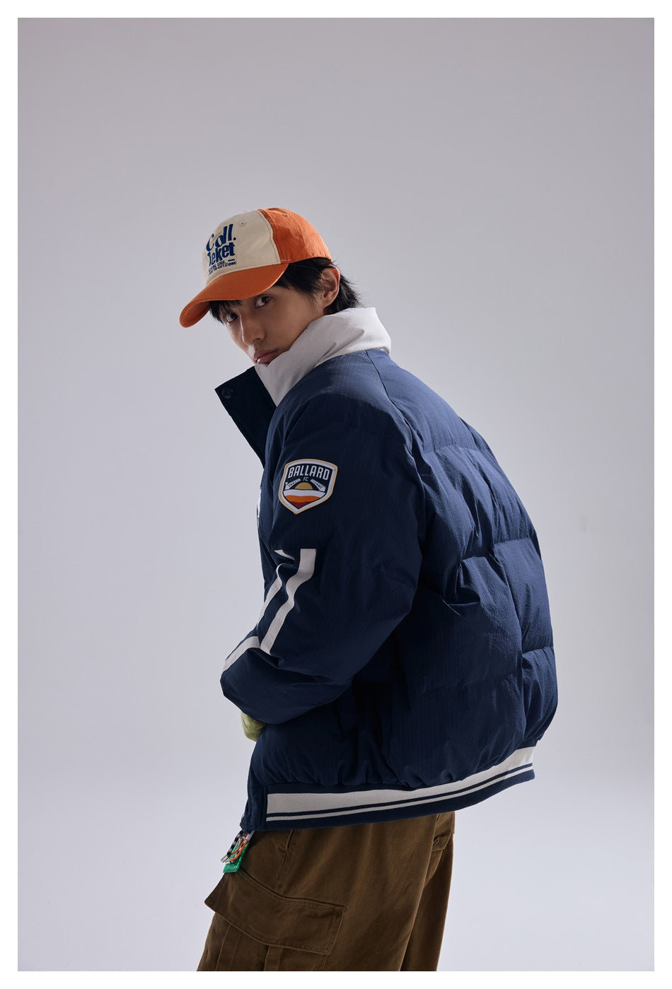 Model looking over his shoulder in a navy puffer jacket, showing its striped sleeve, shoulder patch and ribbed hem.