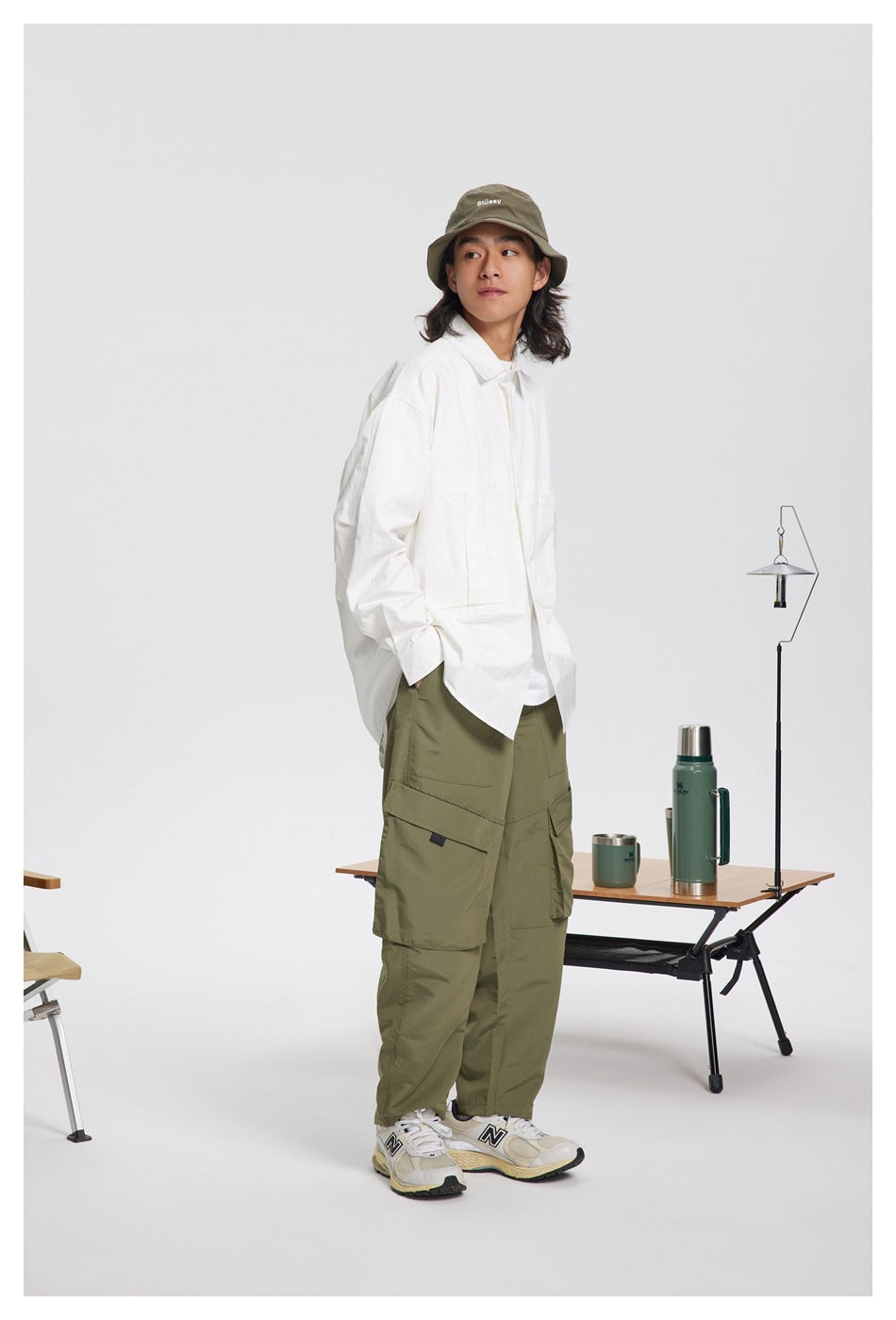 Three-quarter view of a model in a loose white button-up shirt with large front pockets and olive cargo pants.