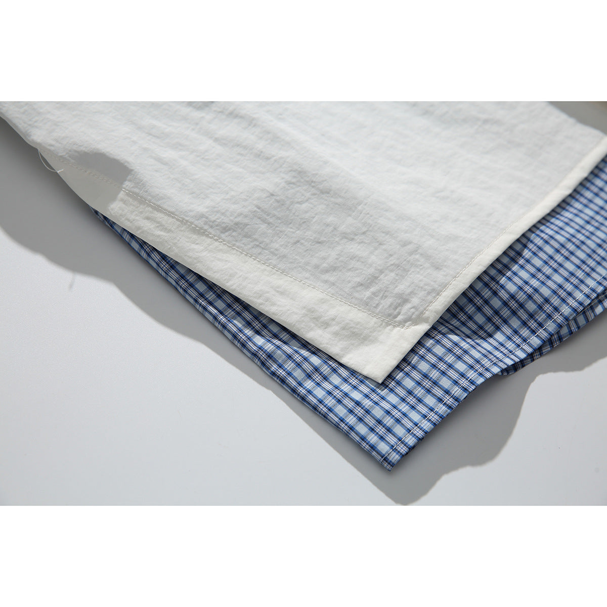 Close-up of an off-white shirt hem layered over blue plaid fabric.