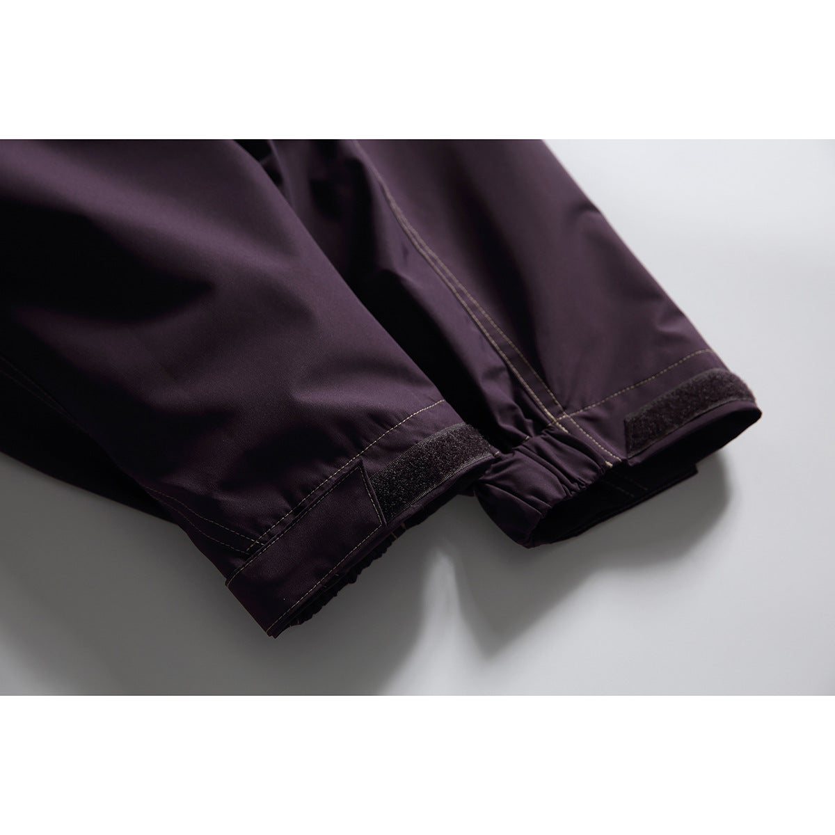 Close-up of the dark plum jacket's sleeve cuffs with hook-and-loop adjustment tabs and contrast stitching.