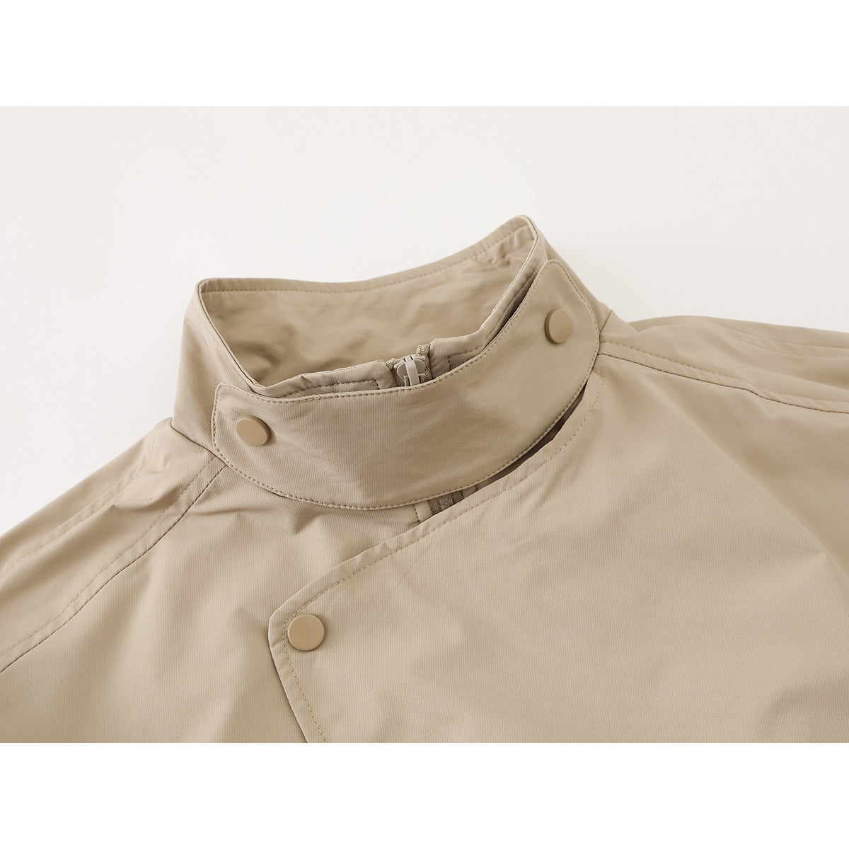 Close-up of a beige jacket’s high stand collar, snap buttons and asymmetrical front closure.