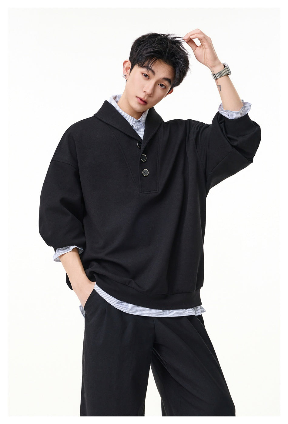 Model wearing a black oversized pullover with a wide collar and three buttons over a checked shirt.