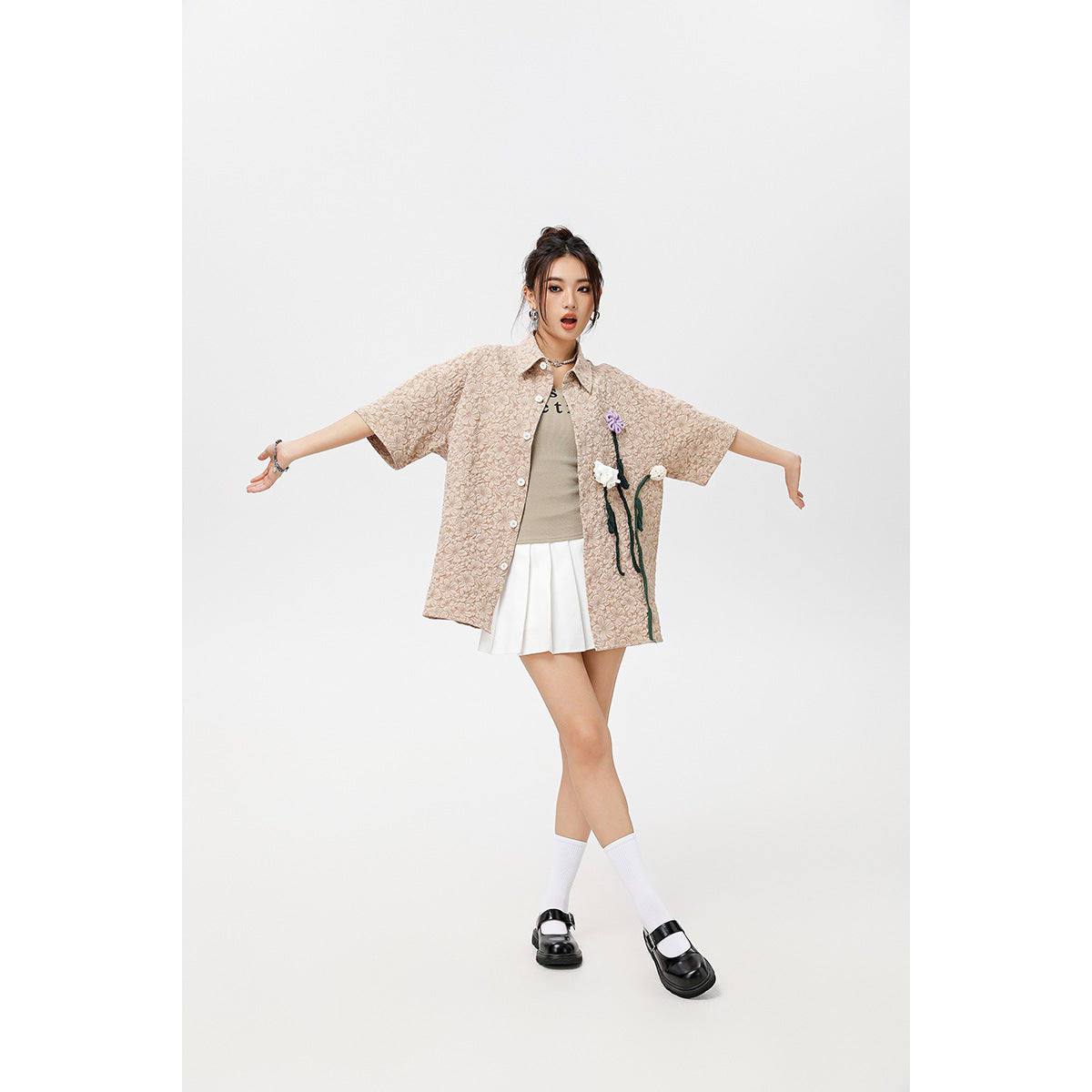 Model wearing a loose beige floral-textured short-sleeve shirt with flower appliqués, a white skirt and black shoes.