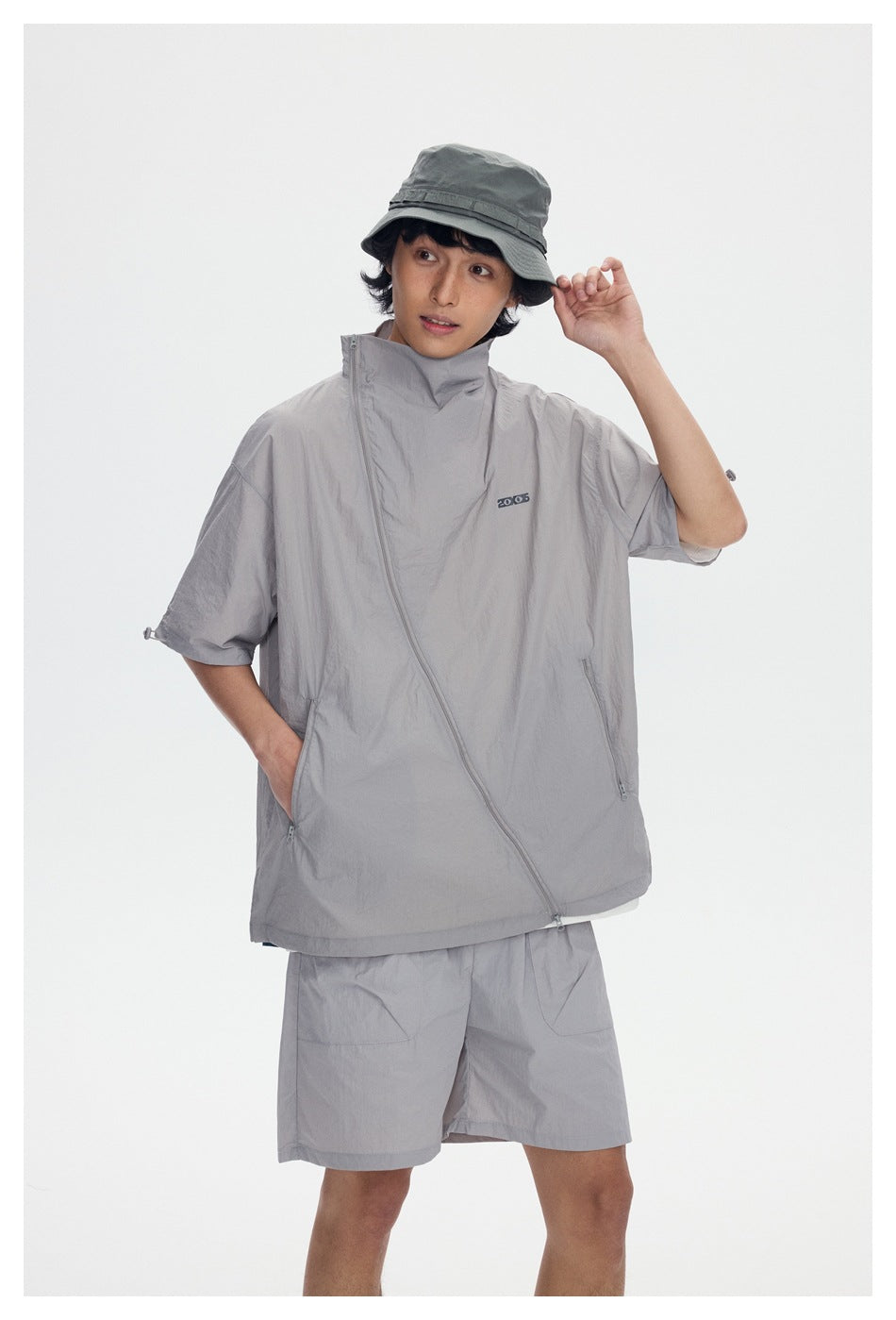 Model wearing a light gray short-sleeve jacket with an asymmetric front zipper and matching shorts.