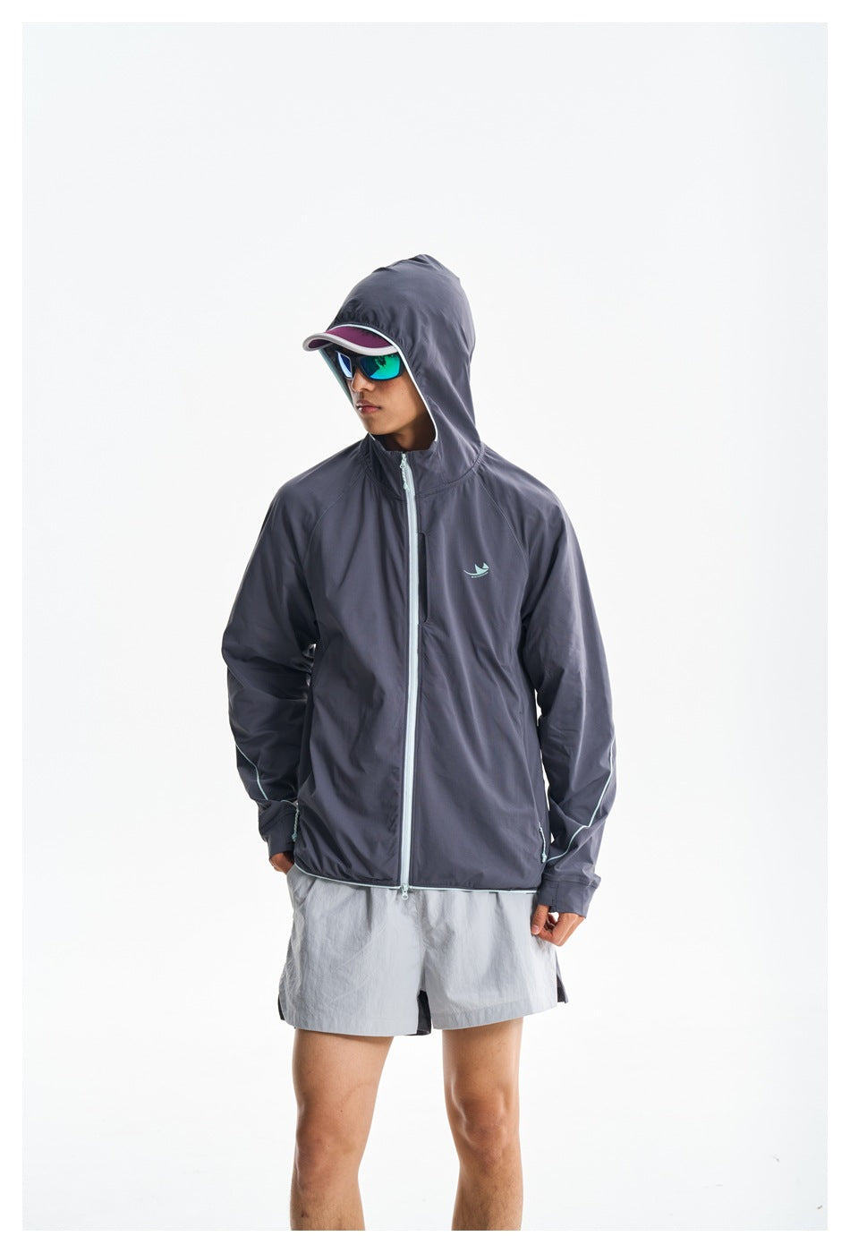 Model wearing a charcoal hooded jacket with pale aqua trim, zipped over light gray shorts.