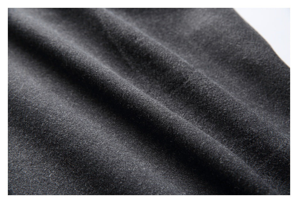 Macro view of the dark charcoal gray trousers' textured fabric and draped folds.