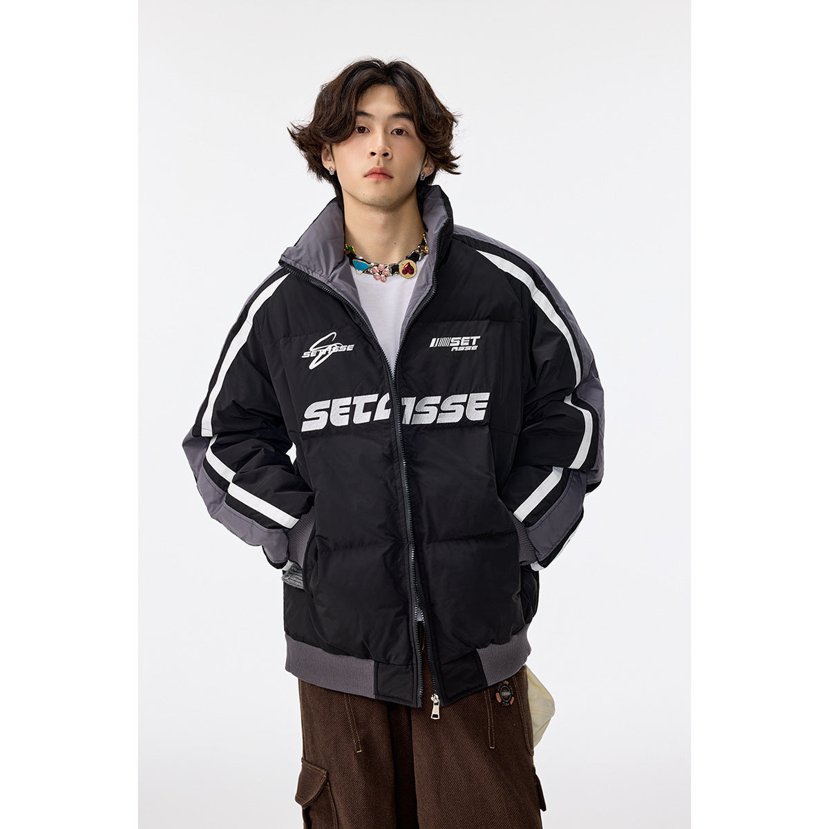 Model wearing a black padded zip jacket with gray panels, white sleeve stripes, a high collar and large white chest