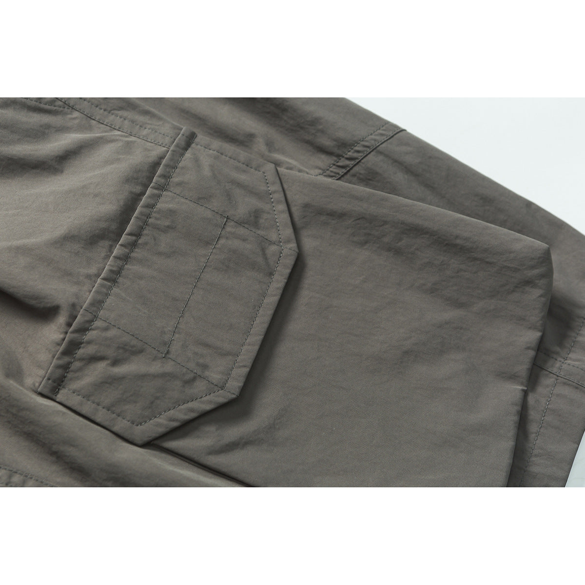 Close-up of gray shorts with a stitched flap pocket and layered seam details.