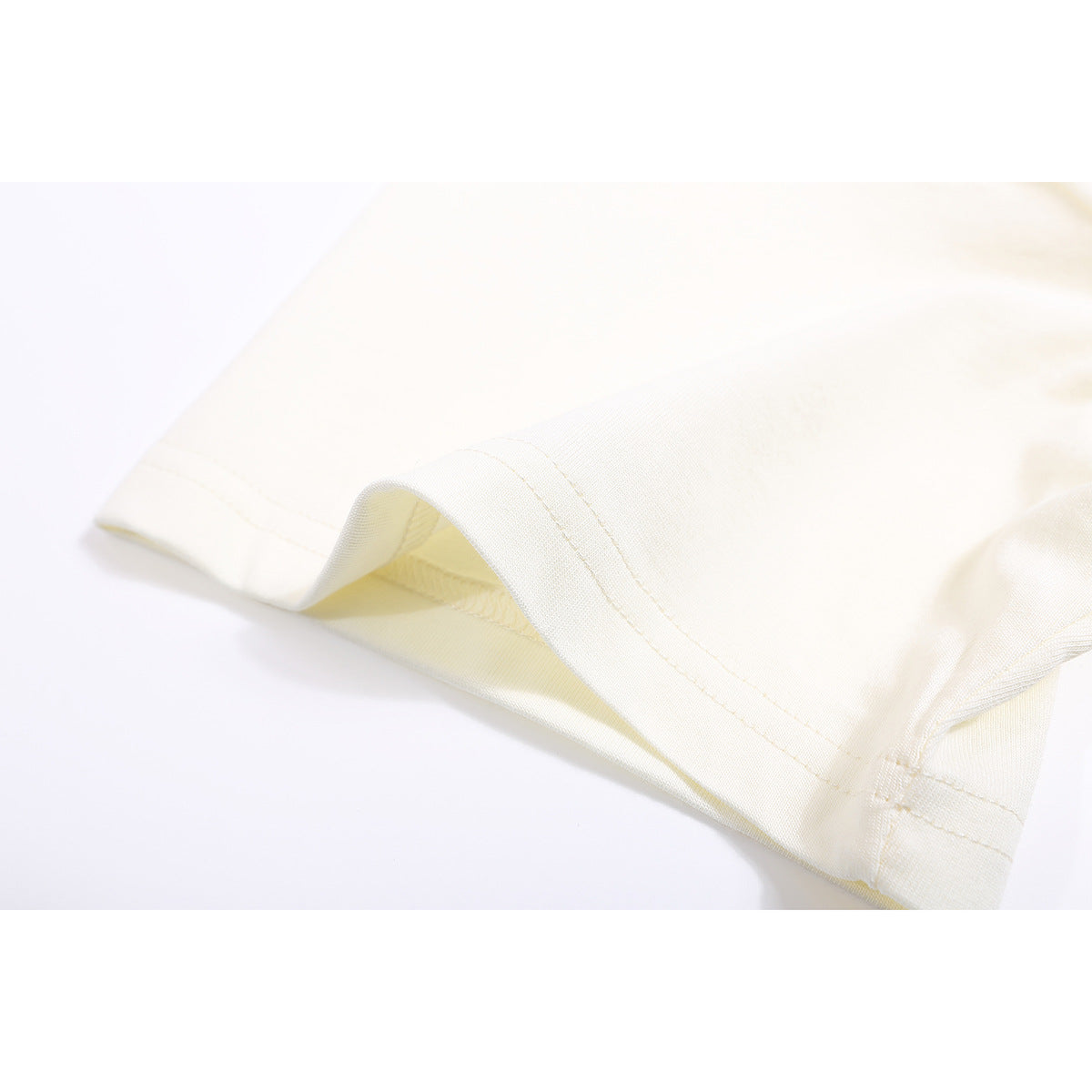 Close-up of the double-stitched hem and fabric of an ivory T-shirt.