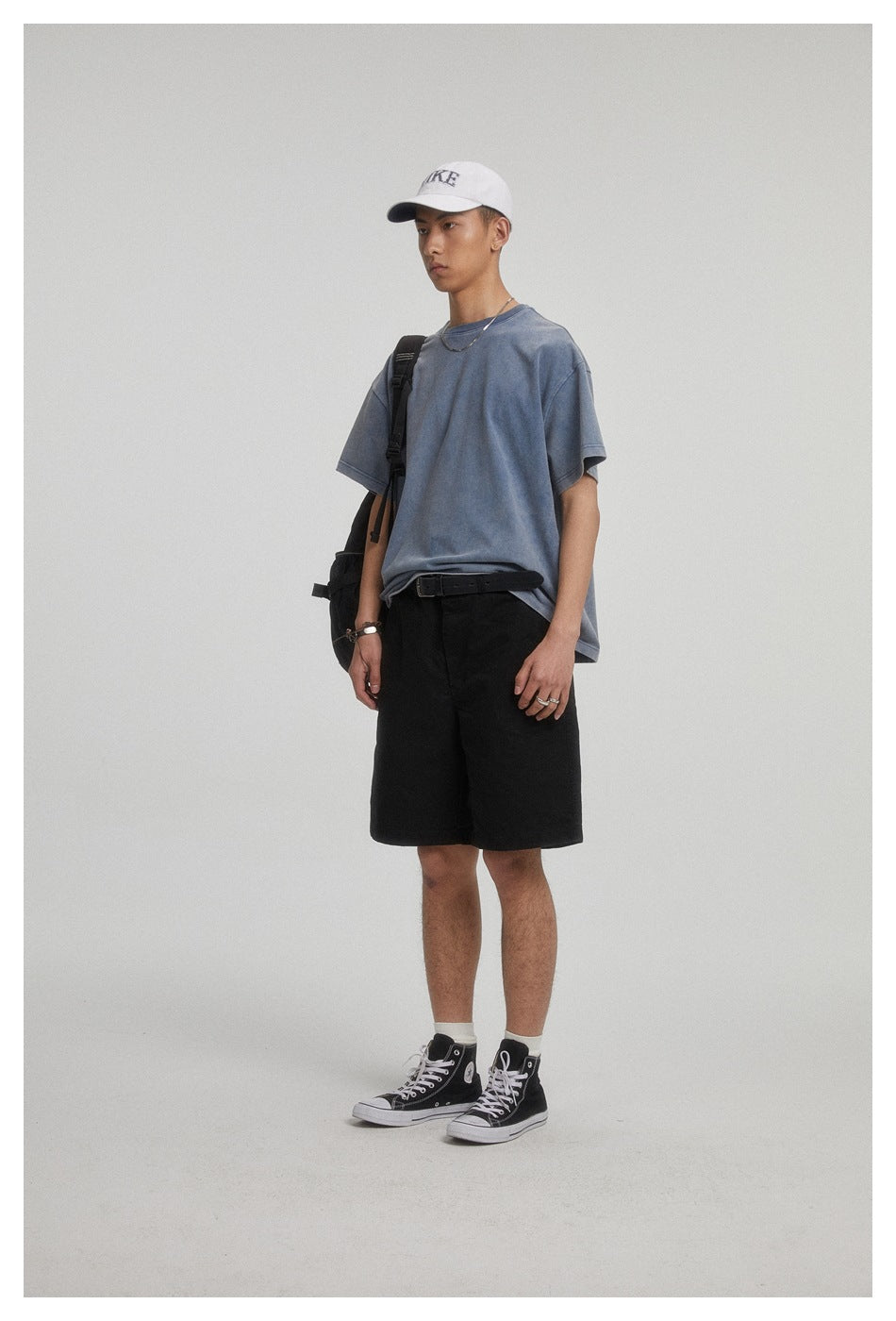 Model wearing black knee-length shorts with a blue-gray T-shirt and white cap.