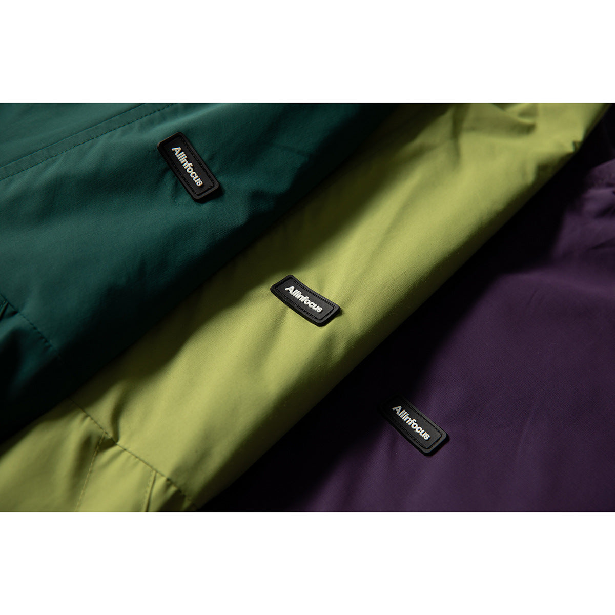 Close-up of dark teal, lime green and purple jacket fabric with small sewn brand patches.