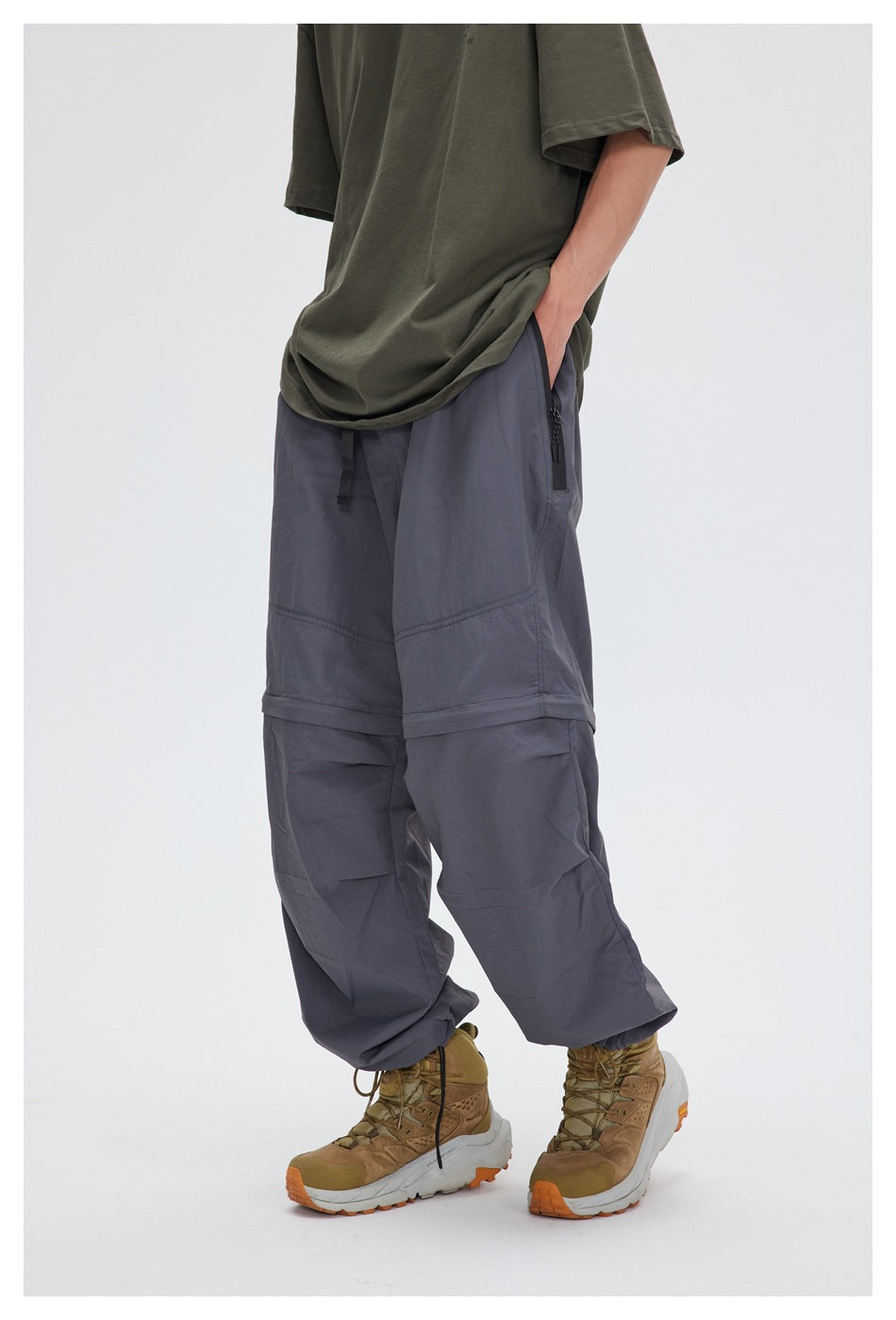 Model wearing gray wide-leg convertible pants with an olive tee and tan hiking boots, hand in pocket