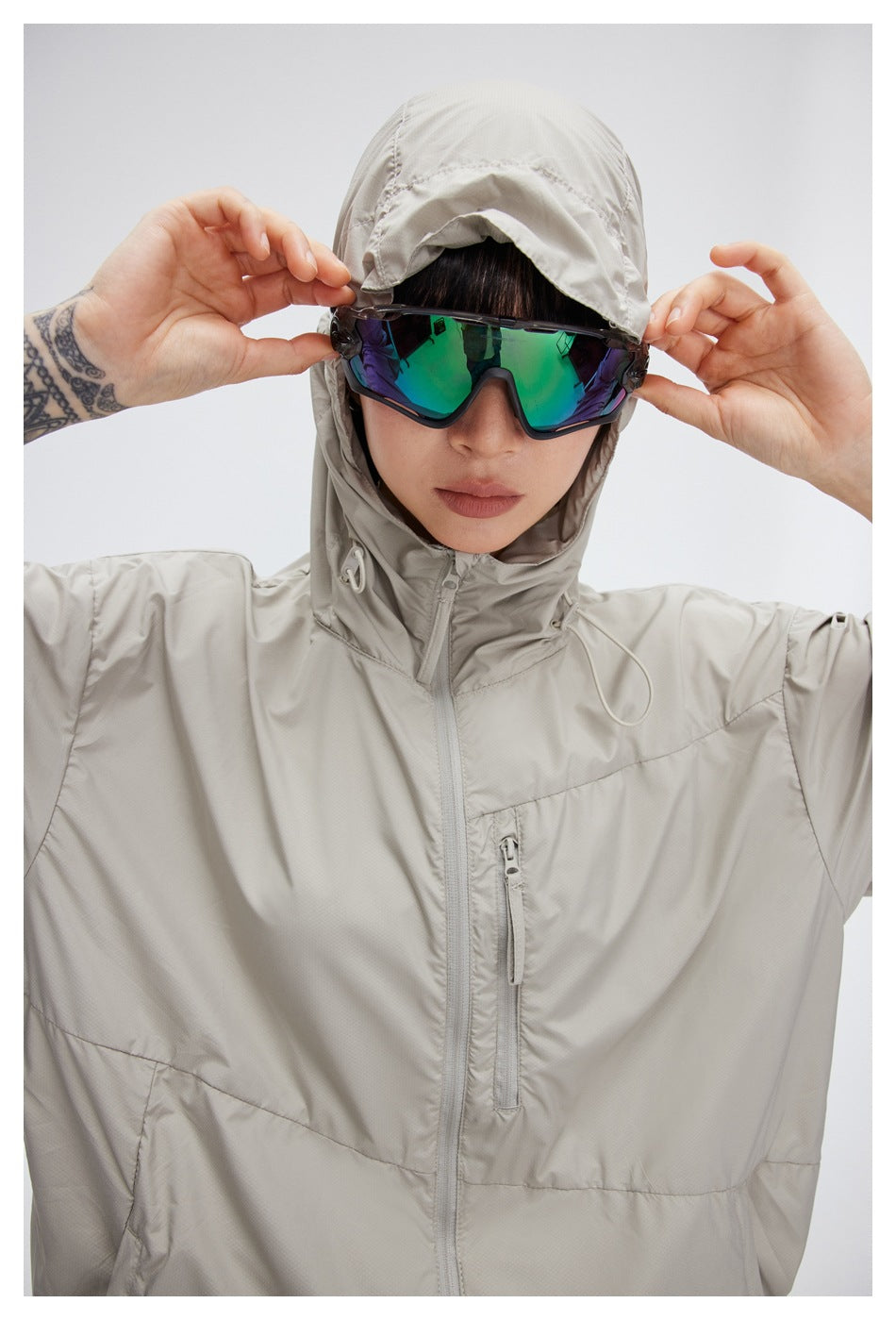 Close front view of a model in a light gray hooded jacket with a zip front and chest pocket.