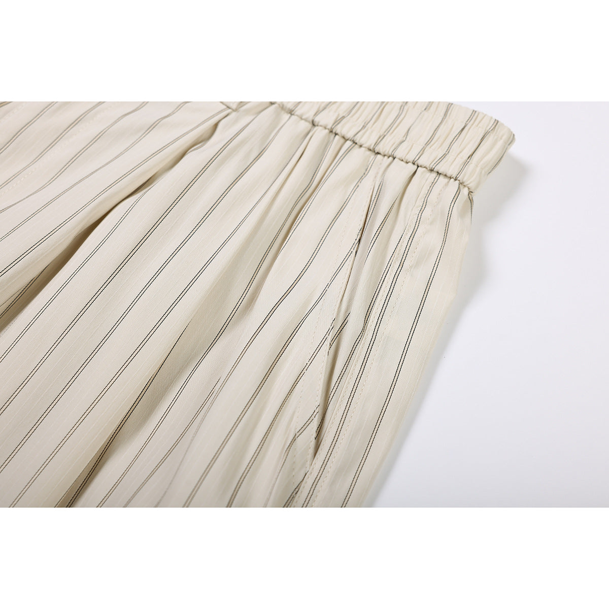 Close-up of cream shorts with thin dark stripes, gathered elastic waistband, and pleated fabric.