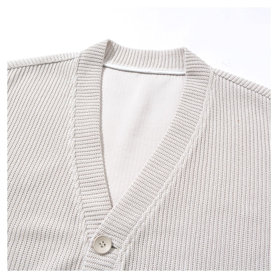 Close-up of a light beige rib-knit cardigan's V-neck opening, button placket, and single button.