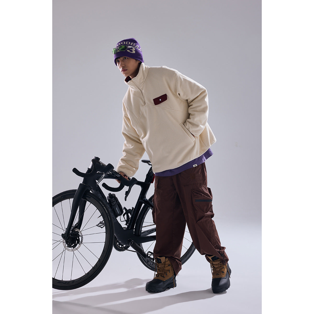 Full-length model wearing an ivory quarter-zip pullover and brown cargo pants beside a black bicycle.