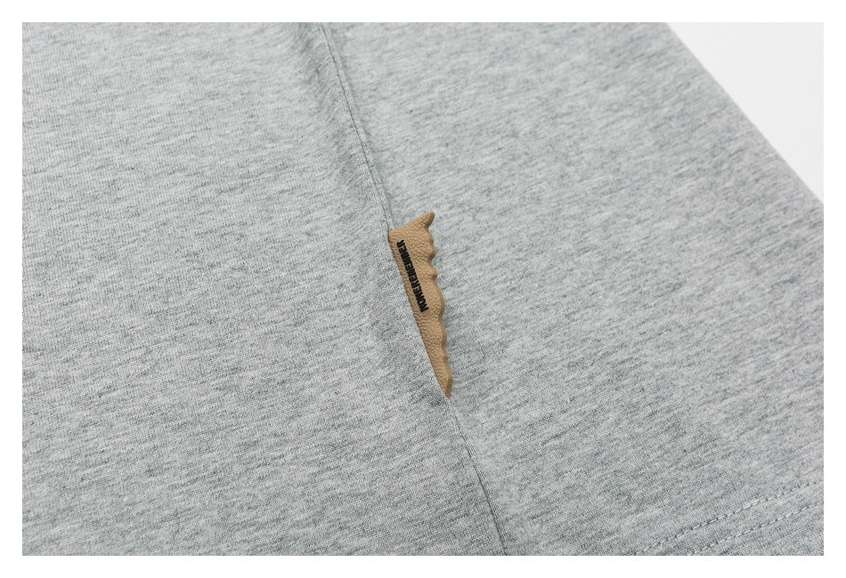 Close-up of gray heather fabric with a stitched seam and a small tan tab bearing dark lettering.
