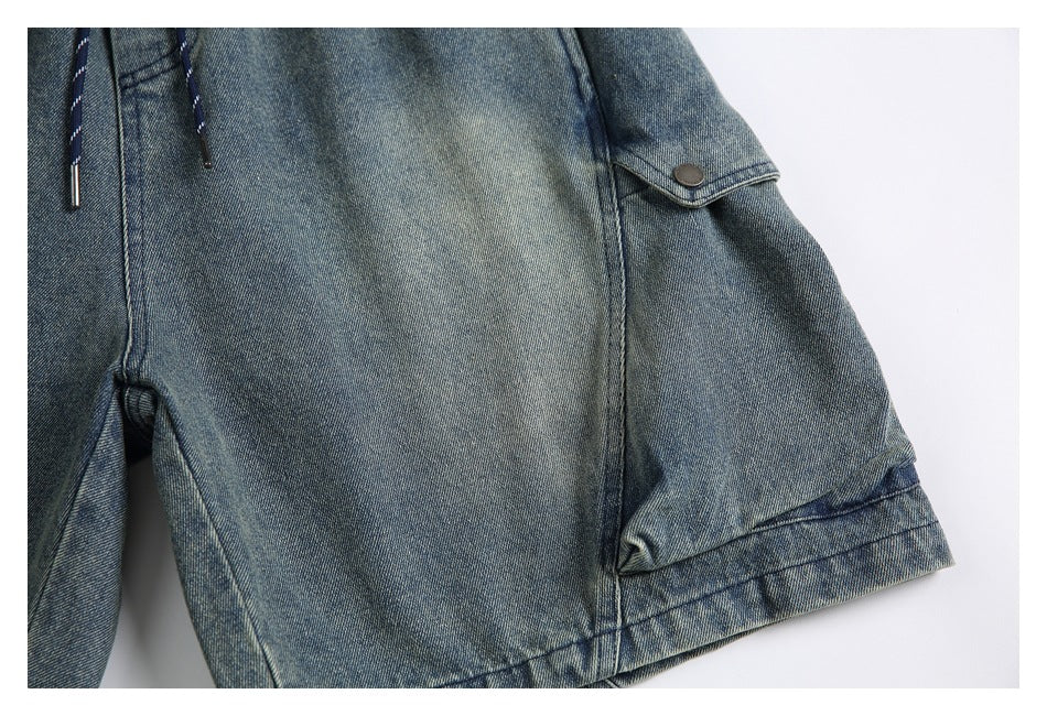 Close-up of a wide shorts leg with a buttoned side flap pocket and stitched hem in blue-gray denim.