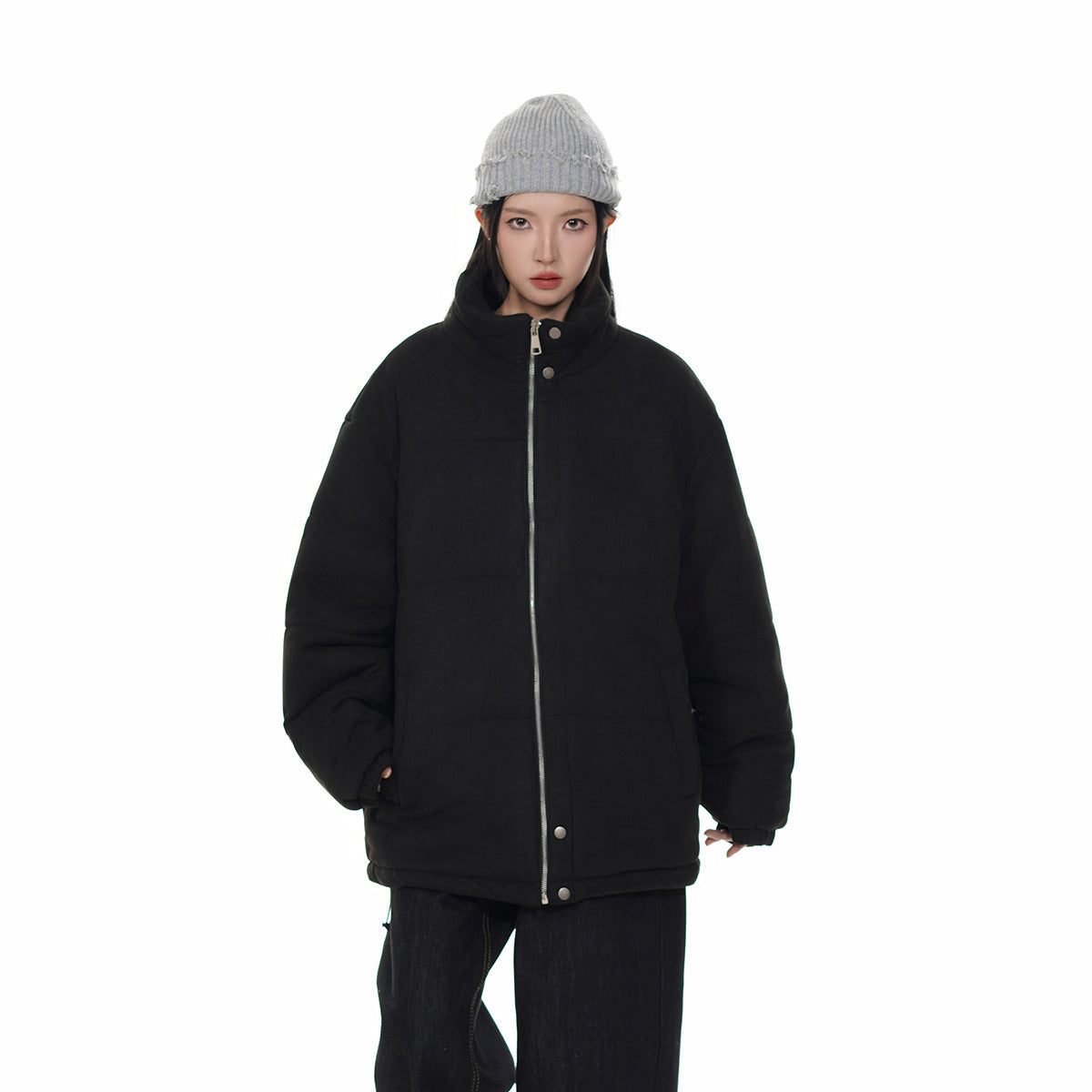 Model wearing a black oversized padded jacket zipped up to its high collar, with a gray knit beanie.