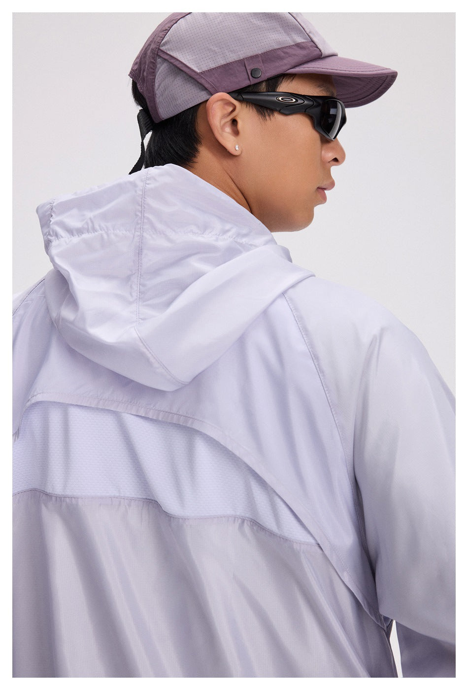 Close-up of the jacket’s hood and curved mesh back panel on a model, with a cap and sunglasses visible.