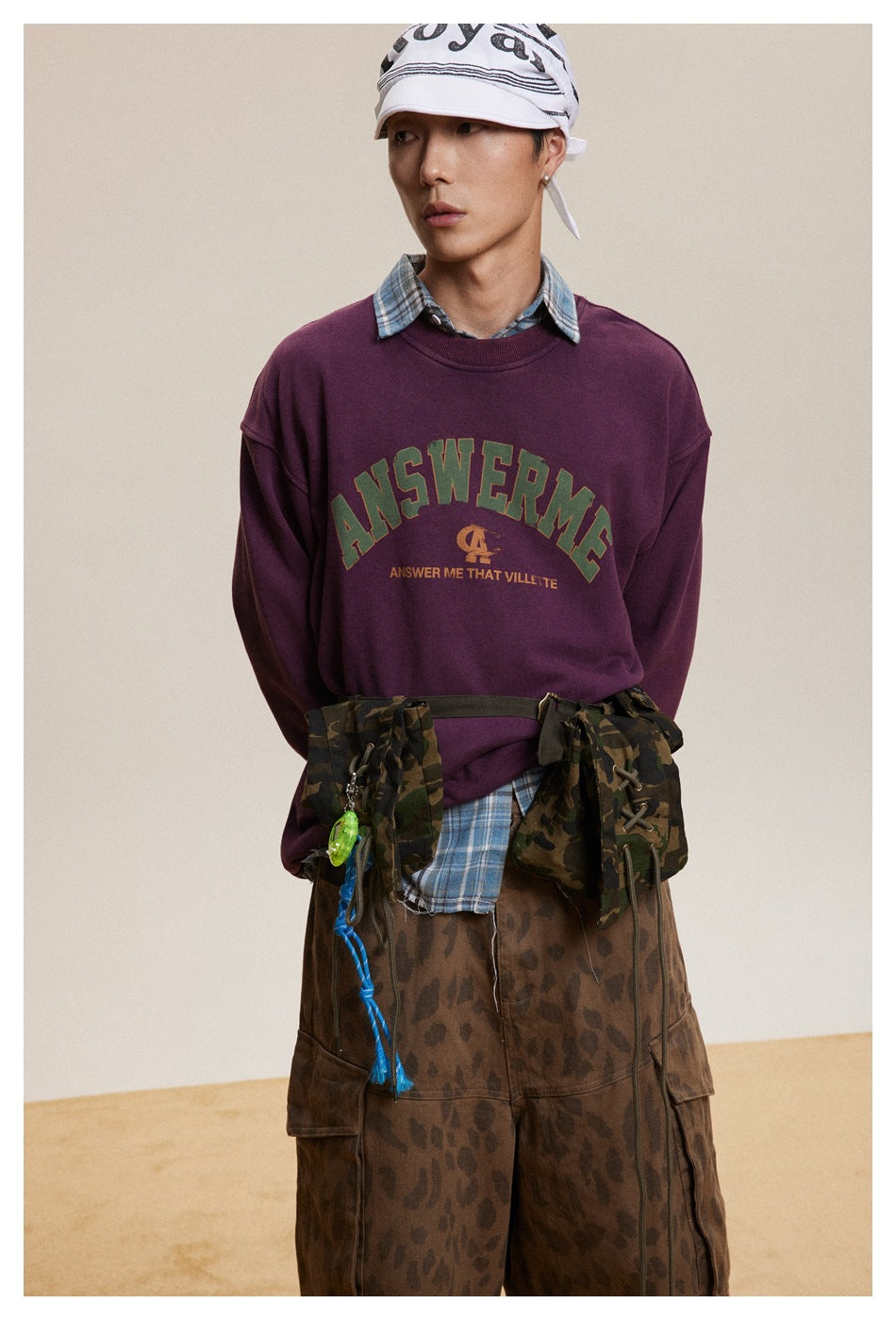 Closer view of a model wearing a burgundy graphic crewneck sweatshirt over a blue plaid shirt.