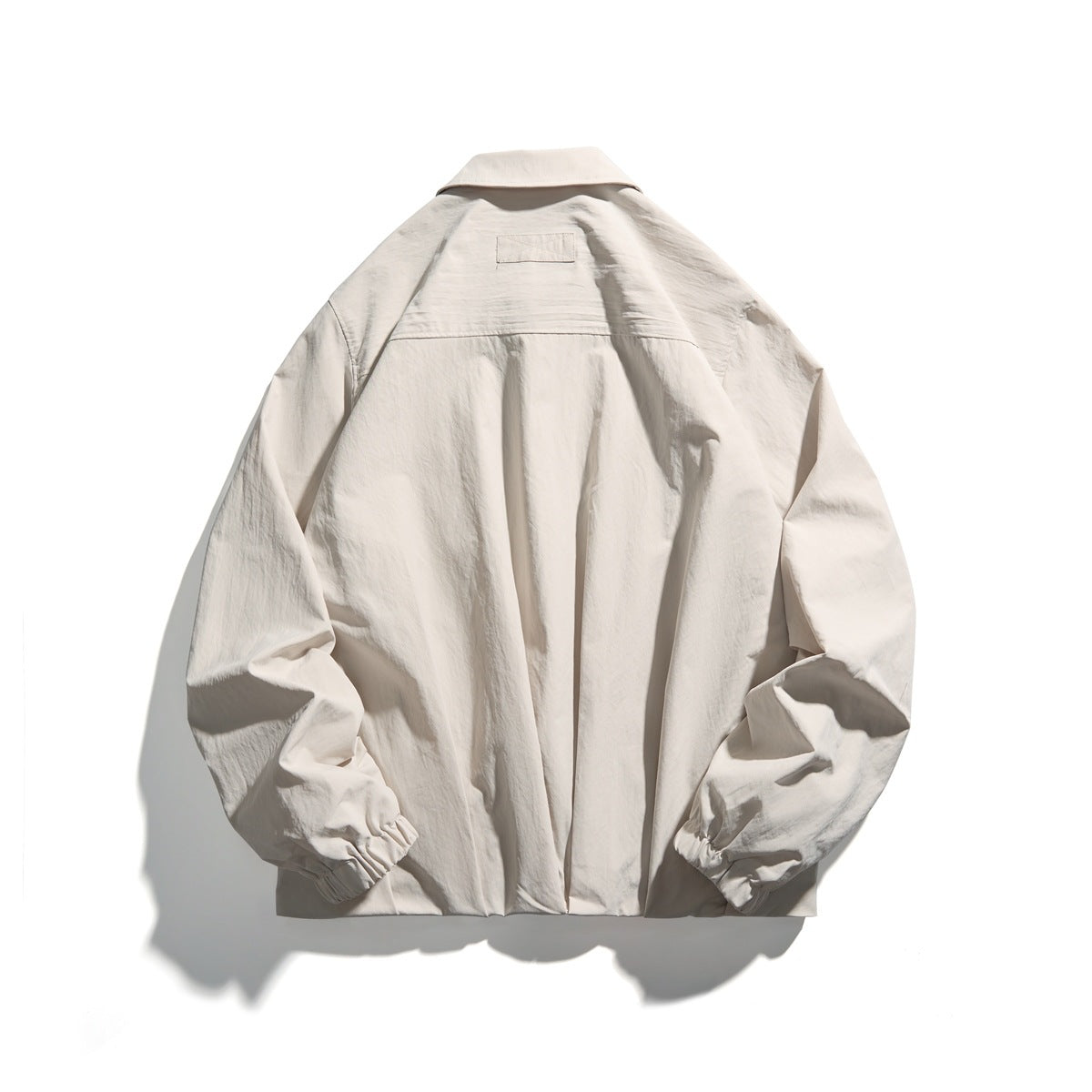 Back view of off-white jacket showing collar, small patch label, back seam and elastic cuffs, flat lay