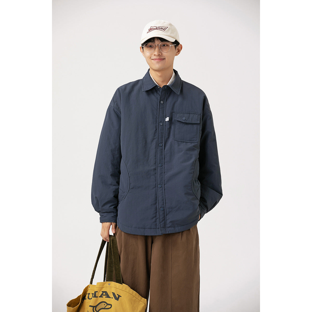 Front view of a model in a navy snap-front jacket with chest and side pockets; a yellow tote is partly visible.
