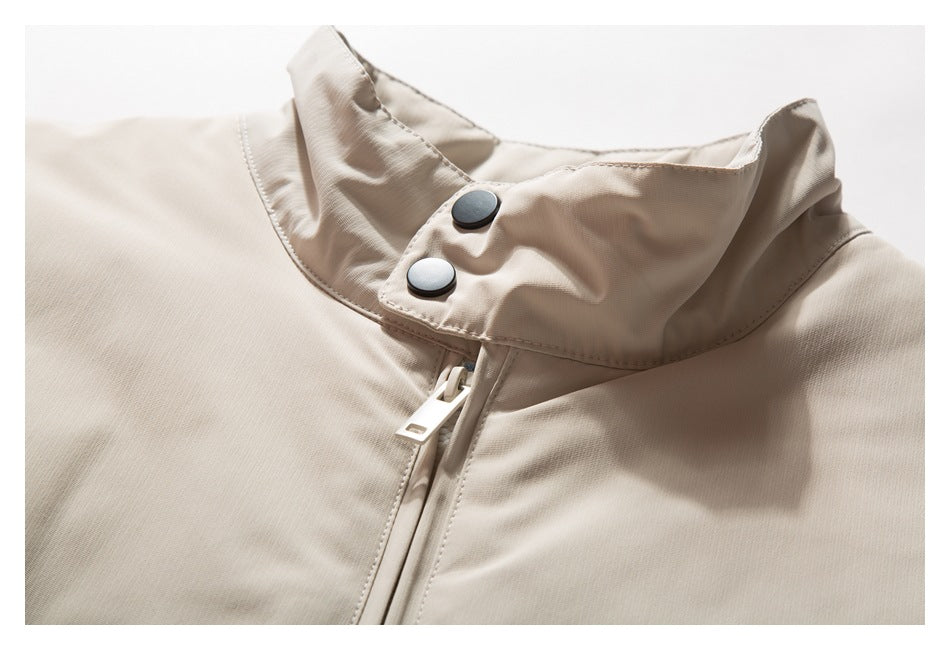 Close-up of a beige jacket's stand collar with two dark snaps and a front zipper.