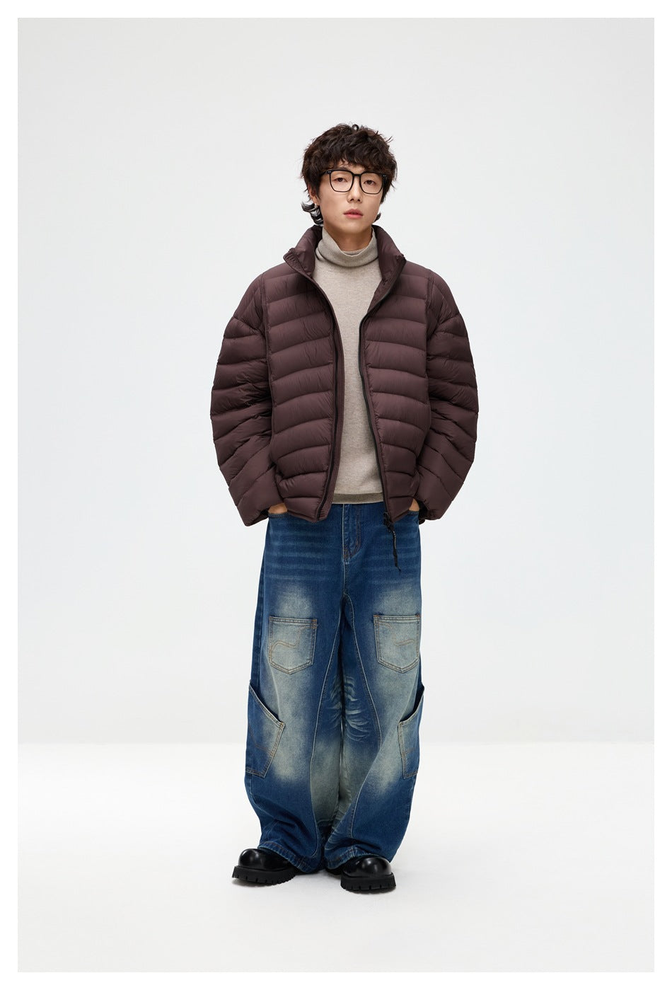 Full-length model wearing a dark brown quilted puffer jacket open over a beige turtleneck and loose blue jeans.