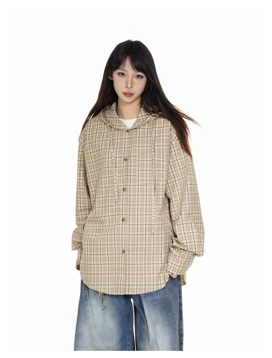 Closer front view of a model wearing a beige plaid hooded shirt jacket with brown buttons and blue jeans.
