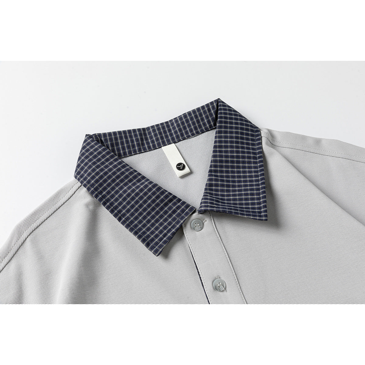 Close-up of a light gray polo shirt with a navy-and-gray checked collar and button placket.