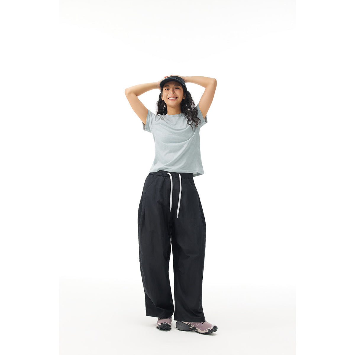 Model wearing a pale gray short-sleeve shirt and loose black drawstring pants, shown from the front.