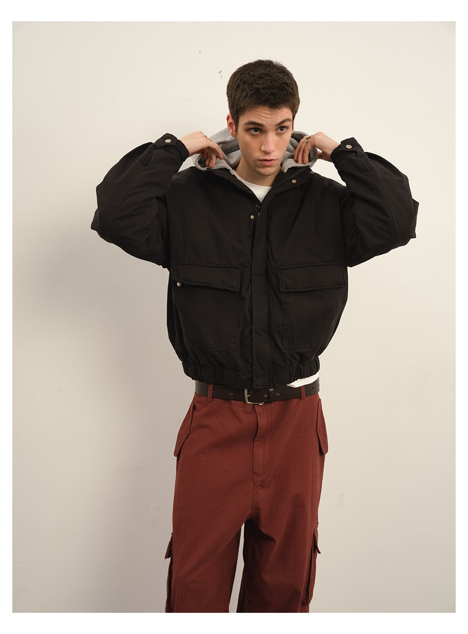 Model wearing a black hooded jacket with snap-front closure, large flap pockets and rust-colored cargo trousers.
