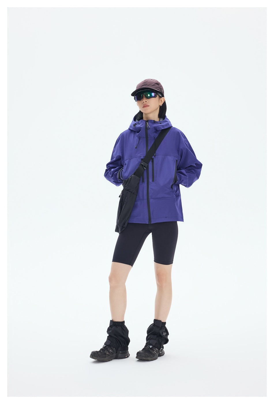Full-length front view of a model wearing a purple hooded jacket with black zippers and a crossbody bag.