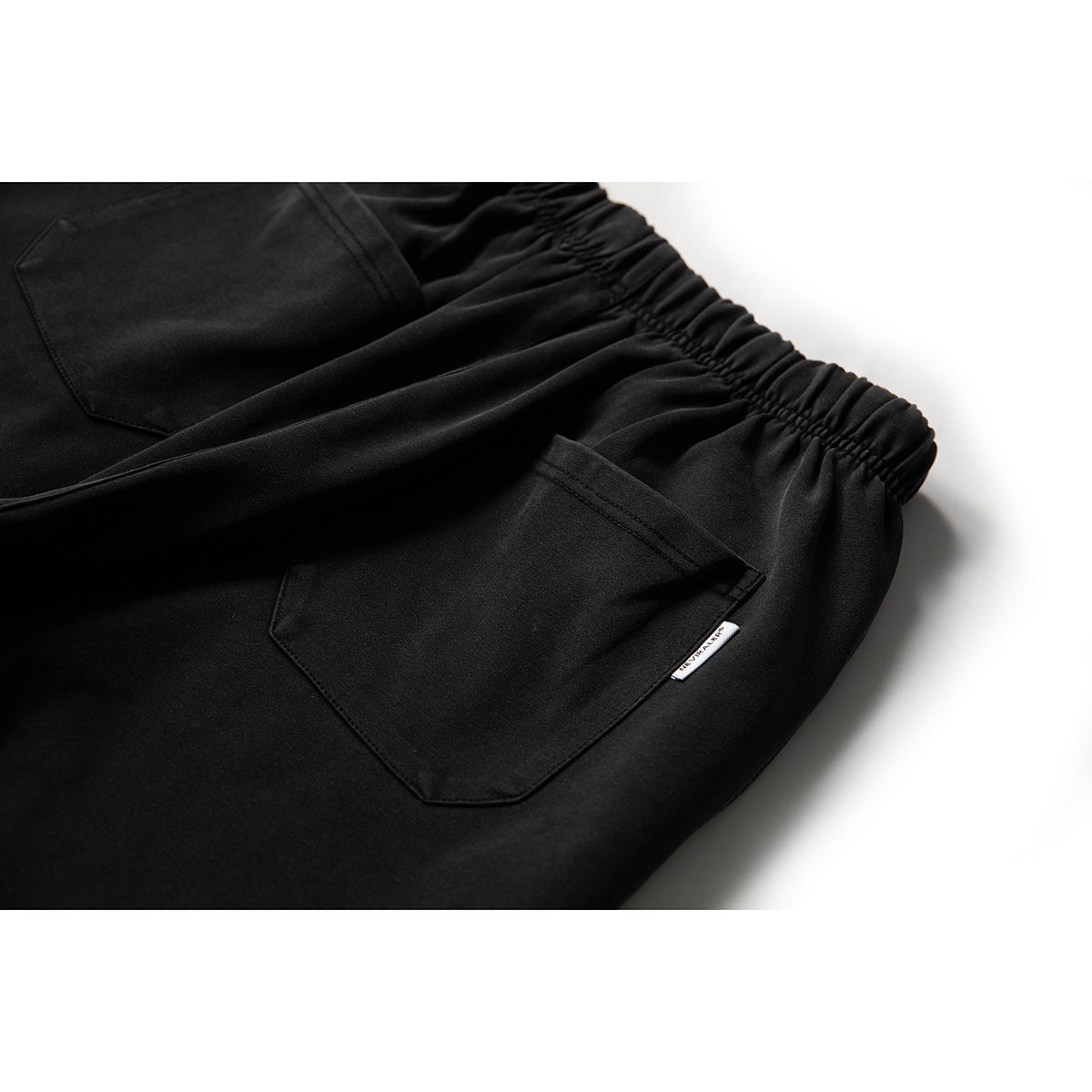 Close-up of black joggers showing the gathered waistband and a large stitched pocket.