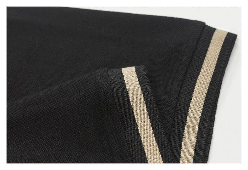 Close-up of a black polo sleeve and cuff with a single beige stripe.