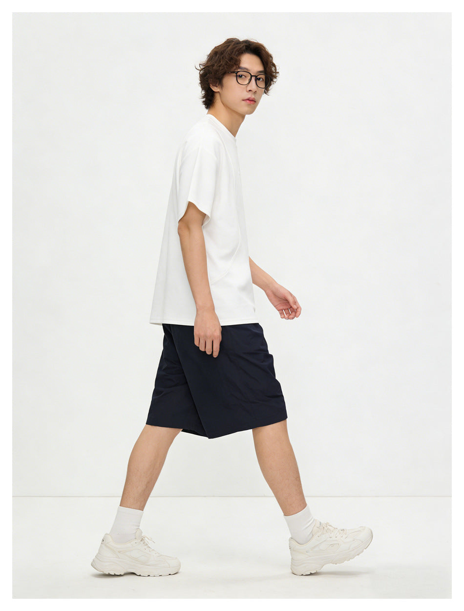 Model in side view walking, wearing a white relaxed short-sleeve T-shirt with navy shorts and cream sneakers