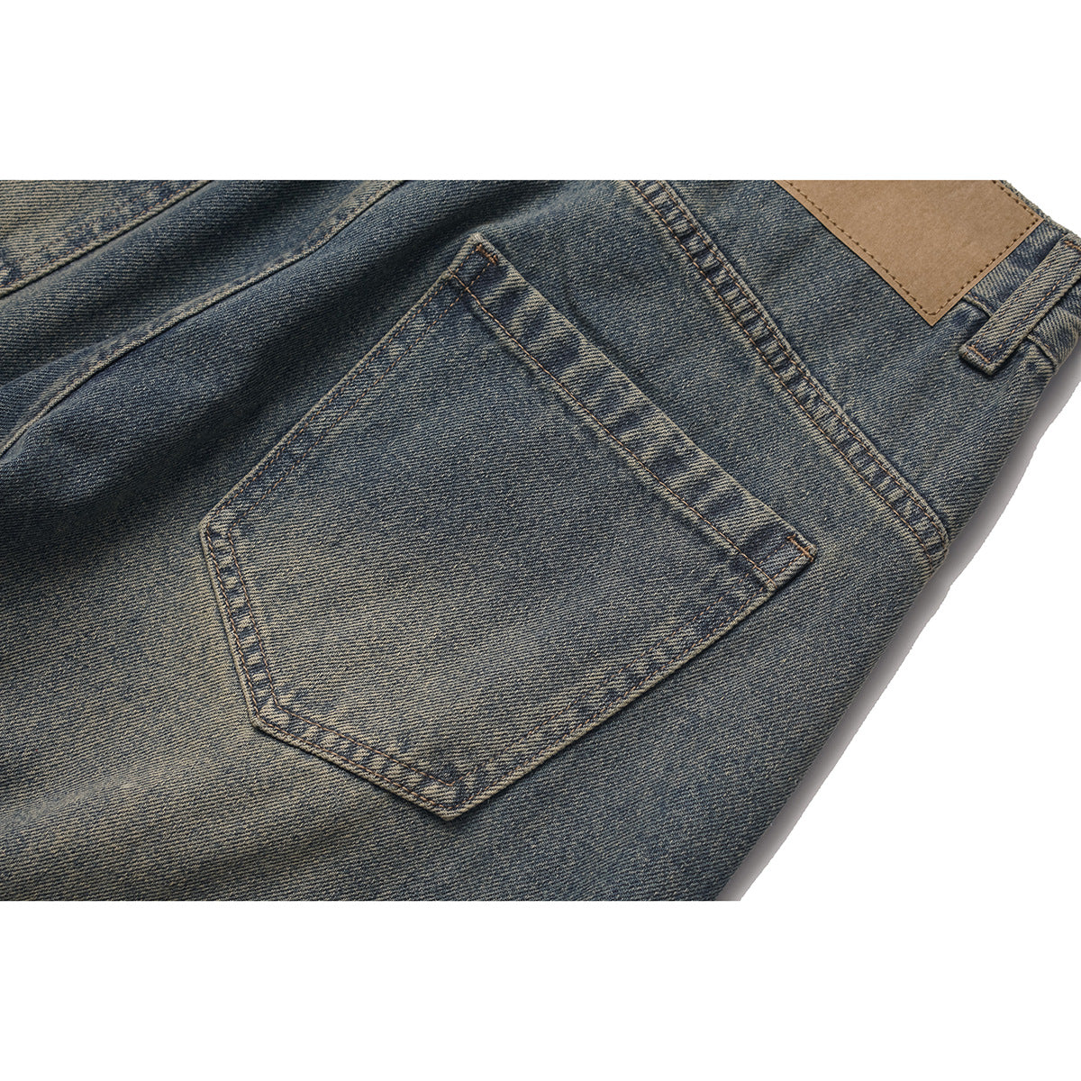 Close-up of a back pocket and plain tan waistband patch on faded dark blue jeans.