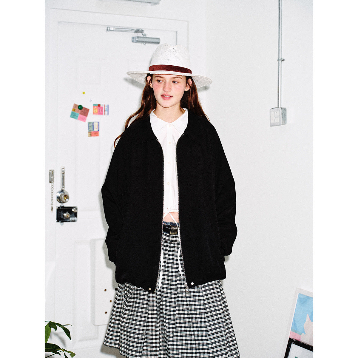 Closer view of a model wearing an oversized black zip jacket over a white blouse and black-and-white checked skirt.
