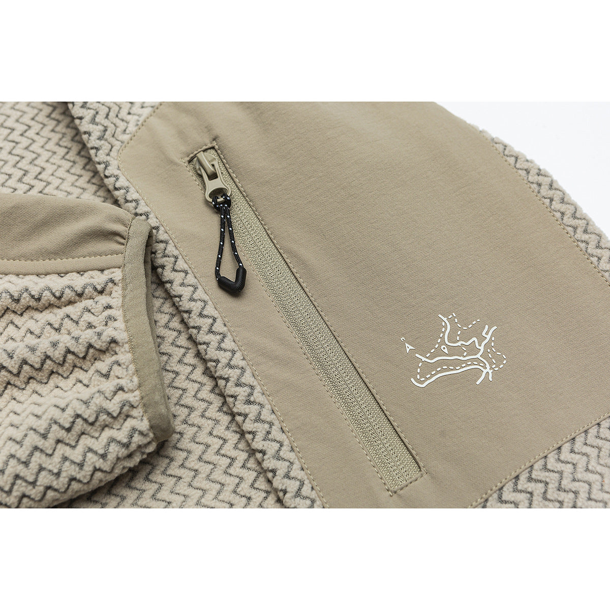 Close-up of a beige jacket's zippered chest pocket, black pull cord, and small white emblem on patterned fabric.