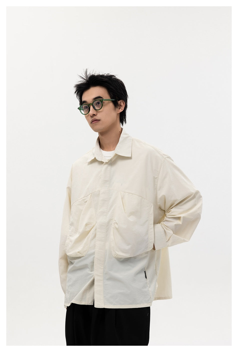 Model in an off-white long-sleeve shirt with large chest pockets and black trousers, hand in pocket, side view