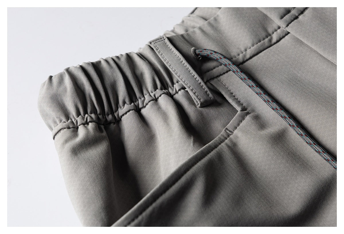 Close-up of gray trousers showing an elastic waistband, belt loop, multicolored drawcord, and pocket seam.