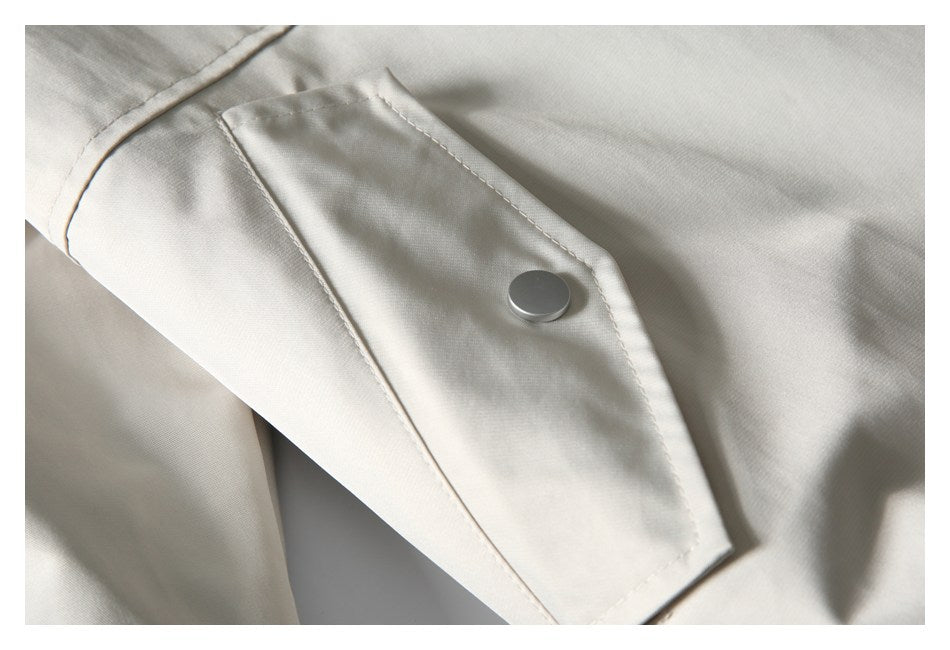 Close-up of an ivory garment's stitched flap and round silver snap button.