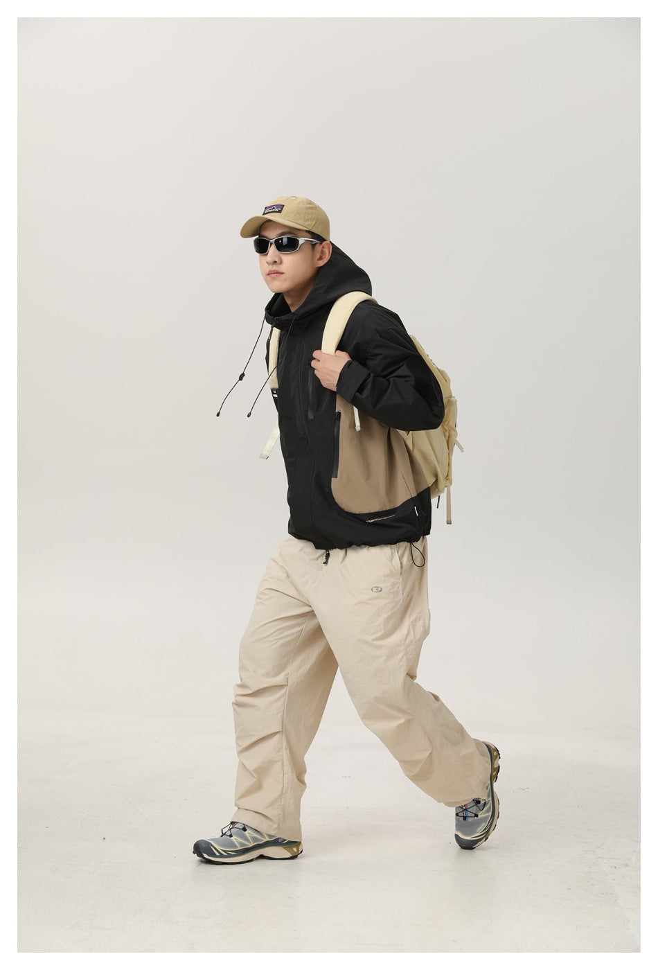 Model wearing a black and tan color-block hooded jacket with beige trousers and a tan backpack.