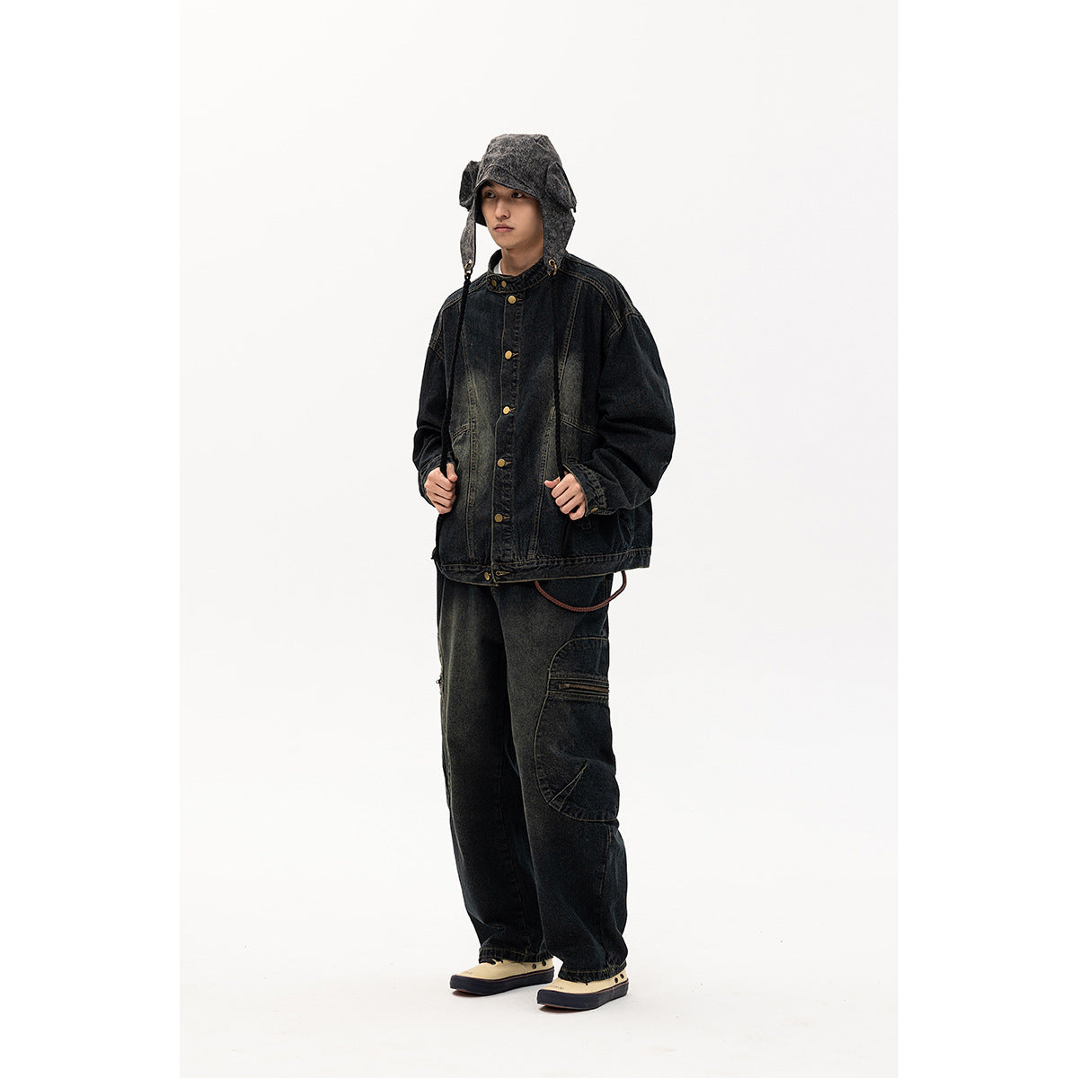 Model wearing a black washed-denim jacket with brass buttons and a matching bucket hat and cargo pants.