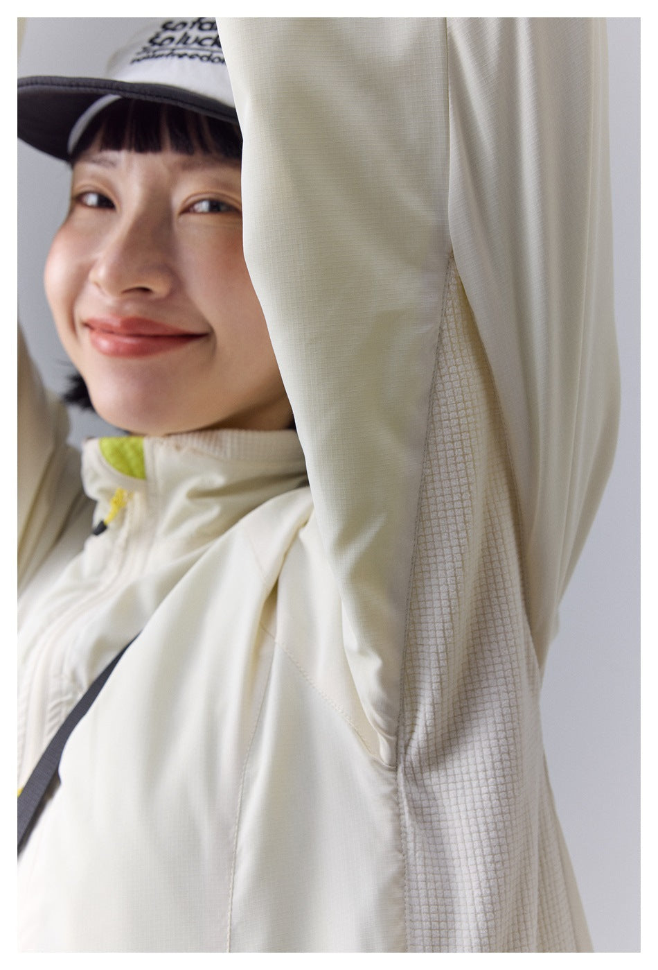 Close-up of a cream jacket's textured underarm panel and sleeve, with part of the model's face and cap visible.