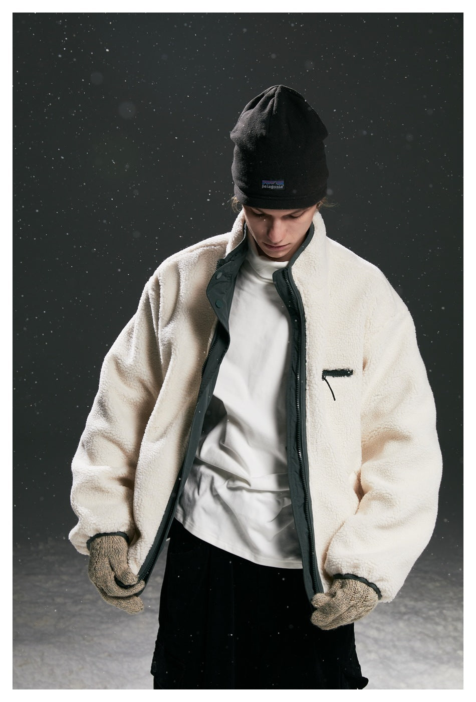 Model wearing an open cream fleece zip jacket with dark trim and chest pocket, black beanie, and knit gloves.