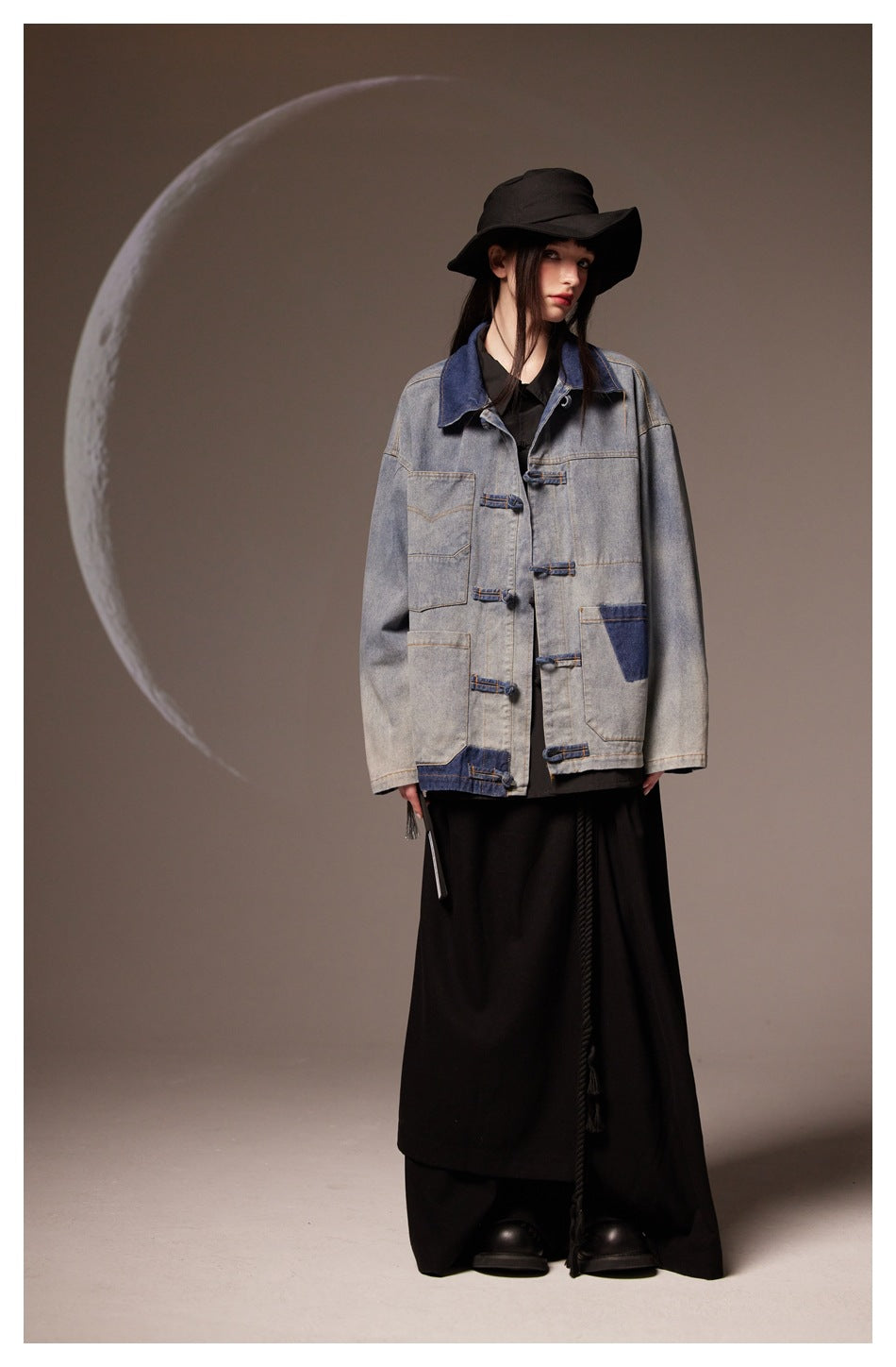 Model in faded blue denim jacket with knotted fasteners and patch pockets, black hat and long black skirt