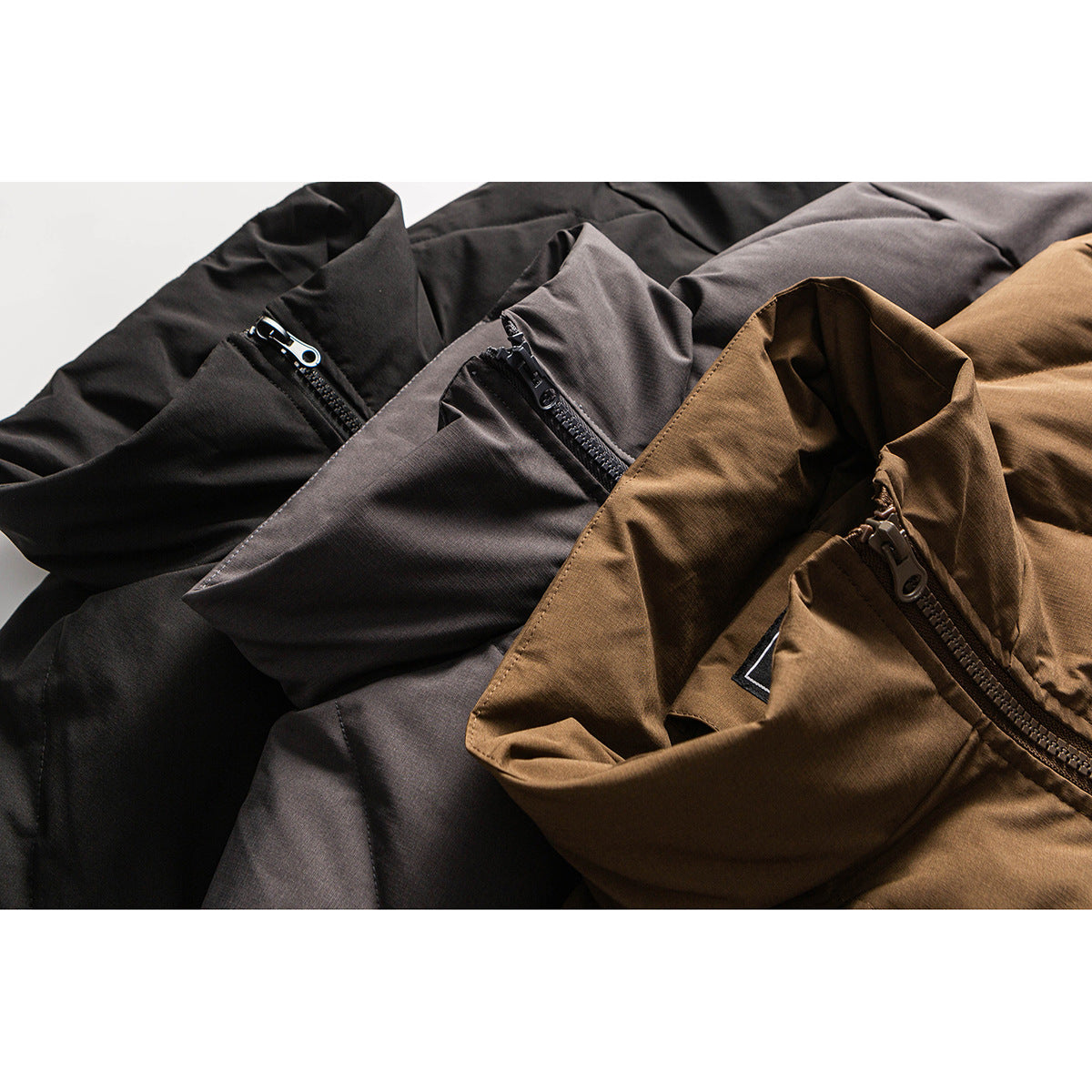 Close-up of black, charcoal gray, and brown jackets showing their front zippers and fabric details.