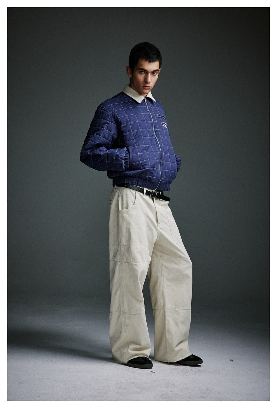 Three-quarter view of a model wearing a navy grid-quilted jacket with cream collar and wide cream trousers.